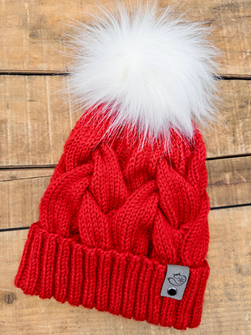 Handmade bright red cable knit pom pom beanie with removable white faux fur pom pom on rustic wood background