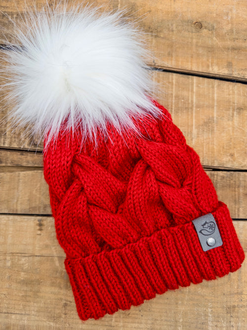 Red knitted beanie with a white fur pom-pom on a wooden surface
